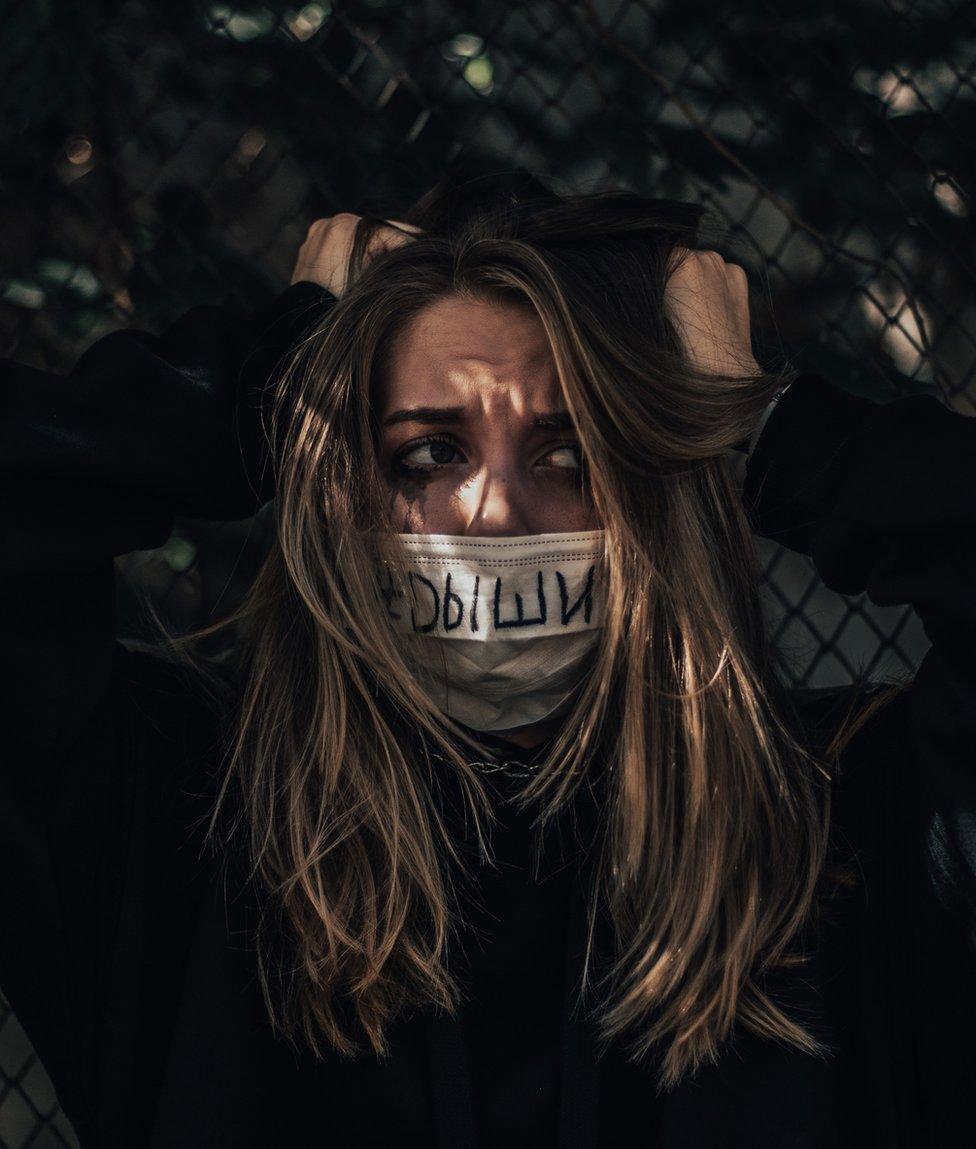 Image of a woman with a mask which has 'breathe' written on it in Russian