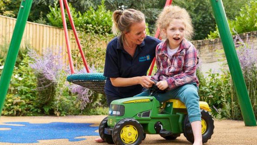 Child on a toy ride-on tractor being helped by a Julia's House employee