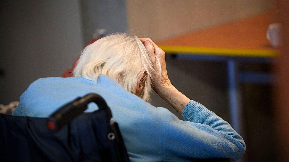 An elderly lady with her head in her hands