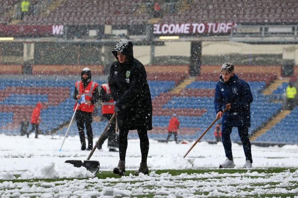 Membersof the ground staff clear snow from the lines as the snow falls ahead of the English Premier League football match between Burnley and Tottenham Hotspur at Turf Moor in Burnley, north west England