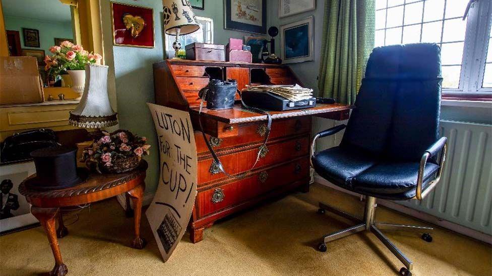 Colour photo of the desk, a 19th Century inlaid mahogany slope front desk, in a study setting