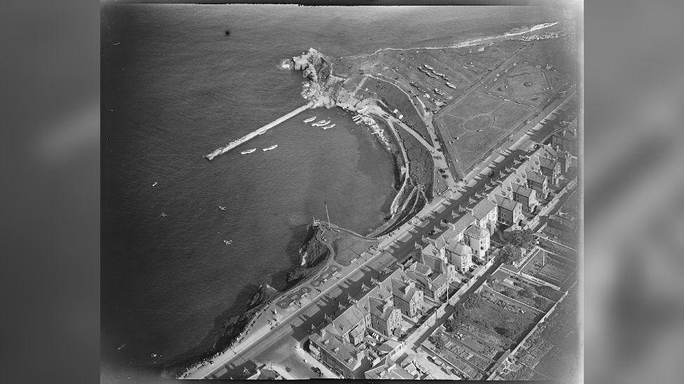 A black-and-white aerial shot of curved beach coastline.