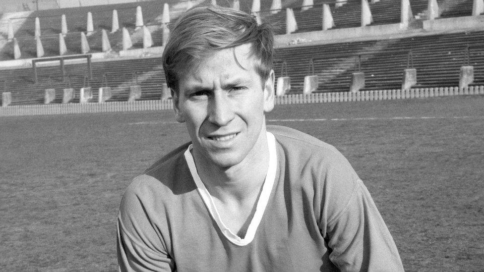 A black and white photo of a young Bobby Charlton on the pitch at Old Trafford