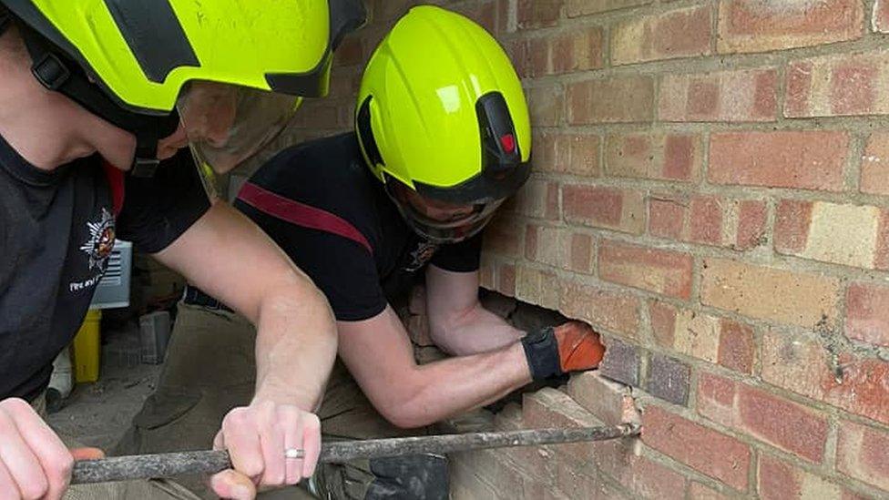 Two firefighters removing bricks from a wall