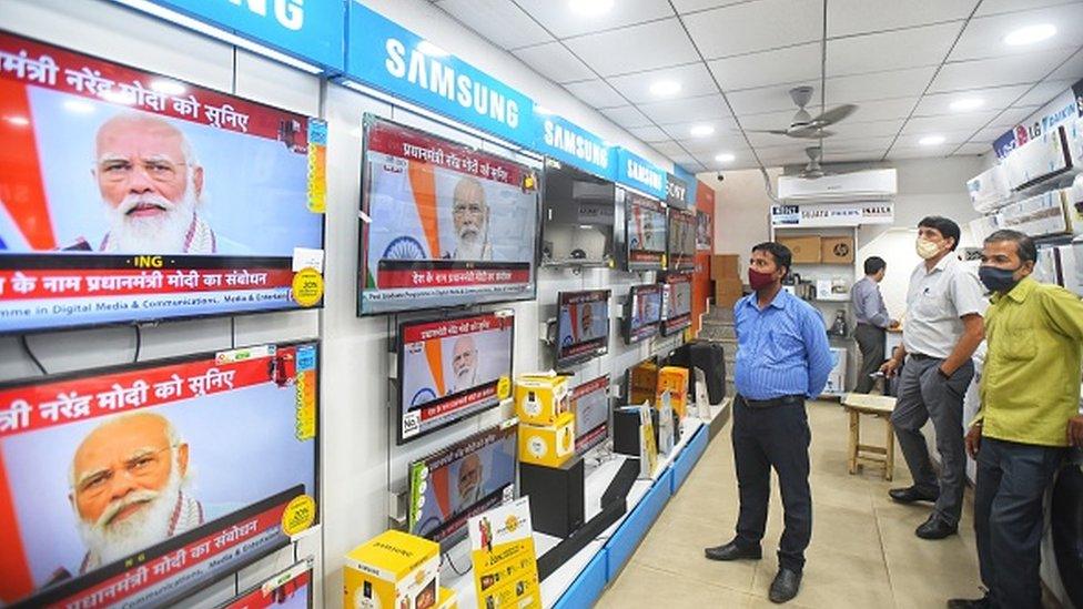 People watch a live telecast of Prime Minister Narendra Modi's address to the nation, at Khanna Market, on October 20, 2020 in New Delhi, India.