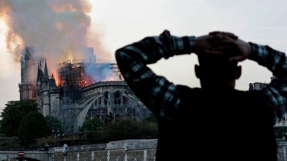 A man watches the landmark Notre-Dame Cathedral burn, engulfed in flames, in central Paris on April 15, 2019