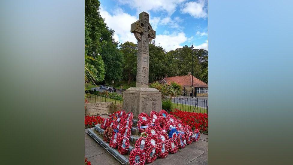 Dozens of poppy wreaths lie at the bottom of a war memorial.