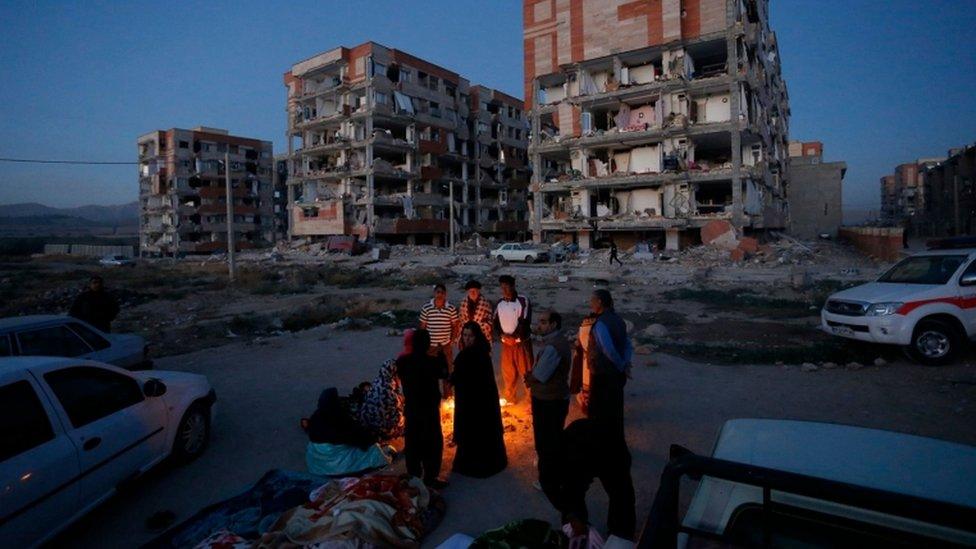 Residents huddle around a fire outside of housing buildings