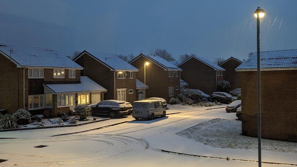 Light shines from a lamp-post in a dark street, illuminating the snowy street below