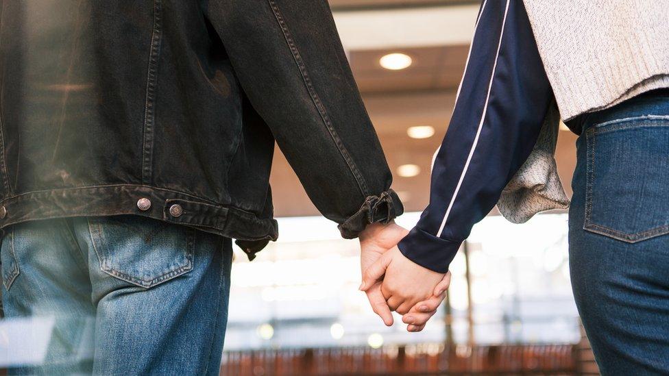 Midsection of young couple holding hands while standing at subway station