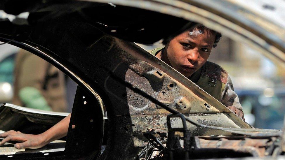 A boy peers through a burnt-out car in Sanaa, Yemen (6 December 2017)