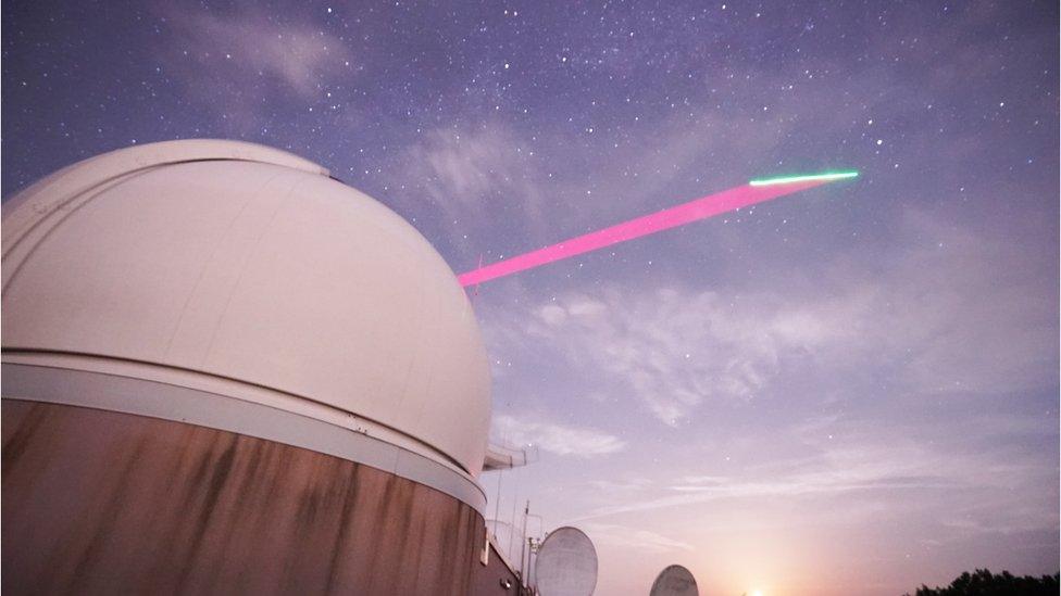 A ground station beams a light signal up to a satellite