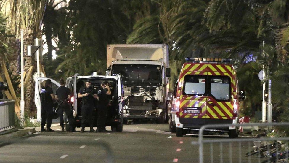 Lorry, riddled with bullet holes, with an ambulance, police van and police officers alongside, at the attack scene.