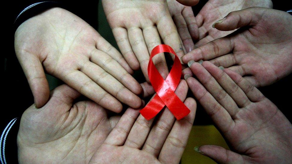 Hands hold a handmade red ribbon to mark World AIDS Day