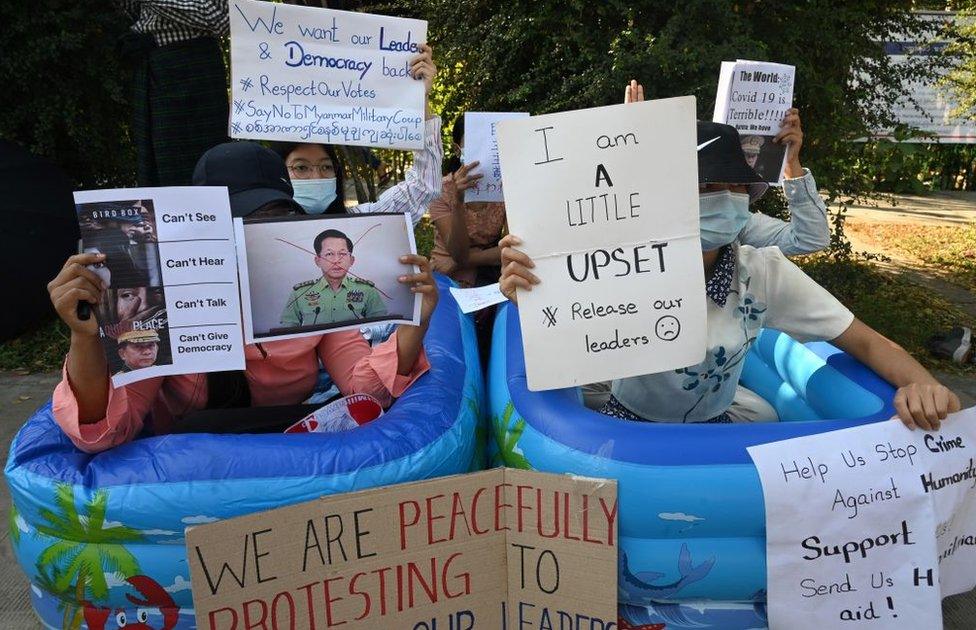 Protesters hold up placards while sitting in plastic tubs during a demonstration against the February 1 military coup