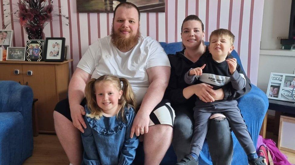 A man and woman pose for a picture on a sofa with two children