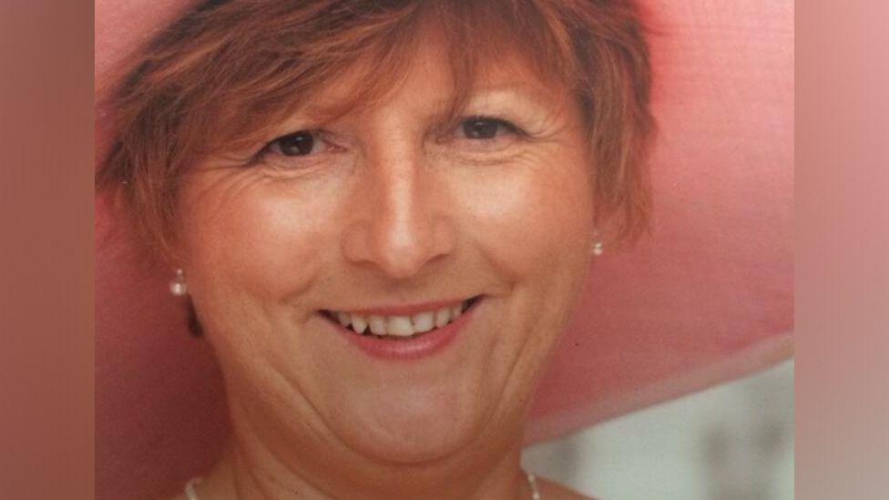 Christine Jones, with short red hair and wearing a wide brimmed pink hat, smiles at the camera.