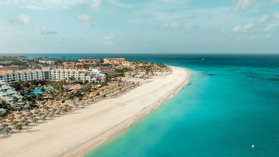 A coastal view of a beach on Aruba with beach umbrellas and hotels and a shimmering blue sea