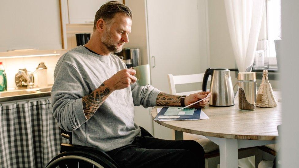 A man in a wheelchair reads a letter at the kitchen table