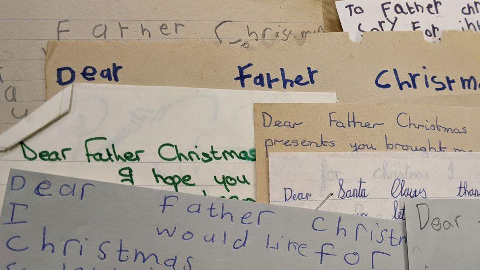 A pile of overlapping letters written by children to Father Christmas.  They are written in blue, green and black ink or pencil. The words Dear Father Christmas can ben seen on five of the letters and there is one letter addressed to Santa Claus 