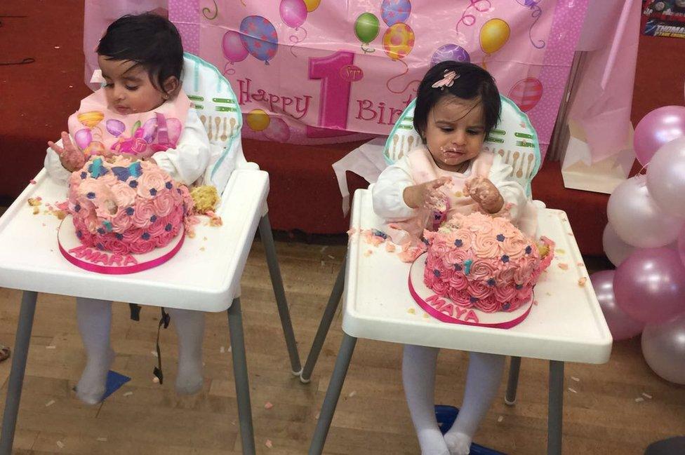 Twins sitting in highchairs eating a cake each