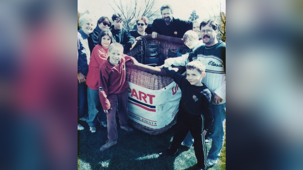 Doug Hoddinott and a group of people surrounding a balloon basket. He is front right, and is aged six