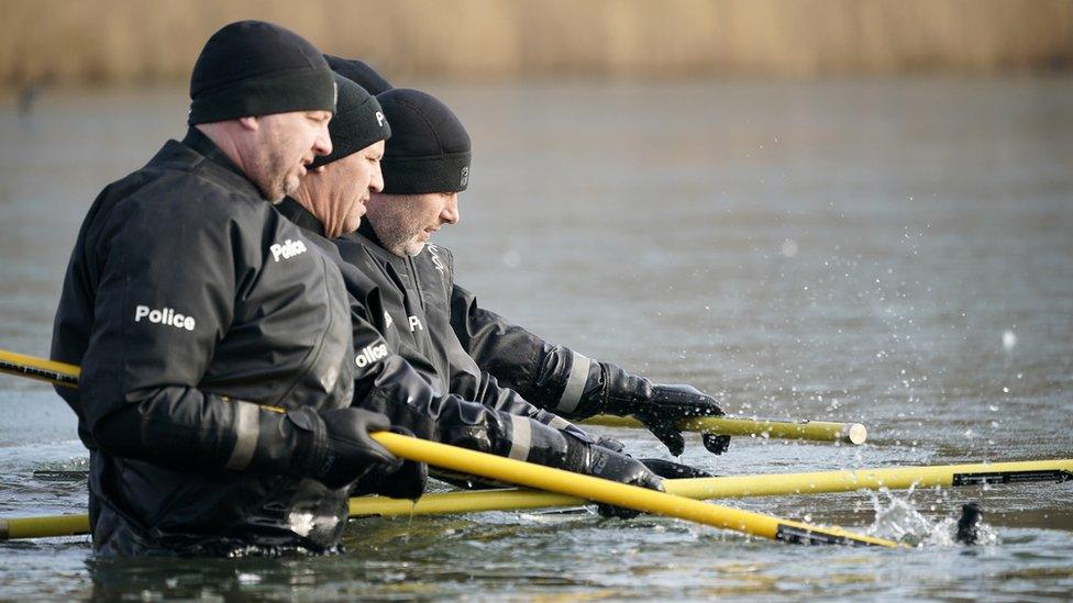 Officers wading through waist-deep pond water