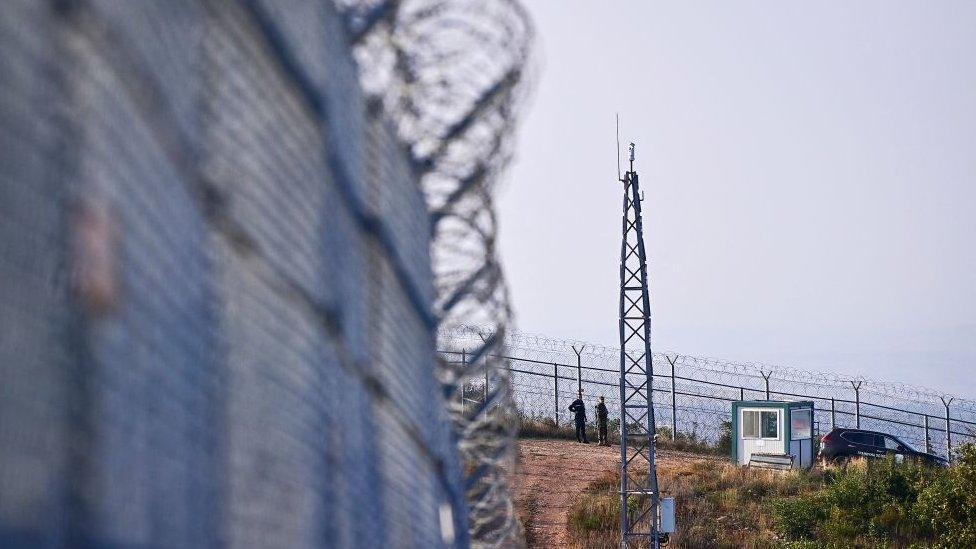 A Bulgarian border police officer (L) stands in position along with a Bulgarian army soldier (R) in front of the border fence on the Bulgaria-Turkey border near the town of Elhovo on September 2, 2022