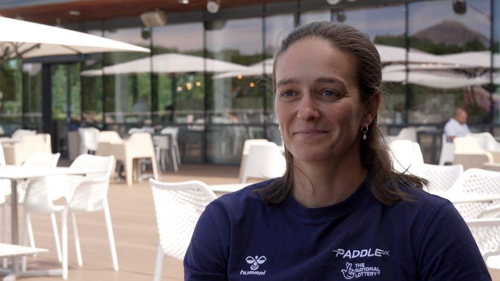 A smiling Mallory Franklin wearing a blue T-shirt sitting in a cafe outside.