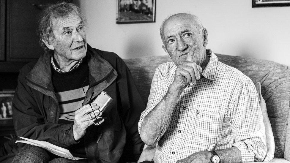 Black and white image of Tony James interviewing Gerald Down. They are both sat on a sofa, looking to the side.