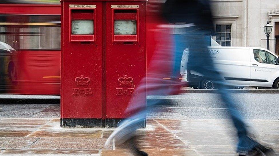 A pedestrian walks past a post box