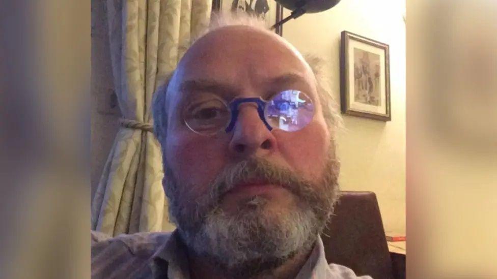 A selfie style photo of a bearded man in glasses at home