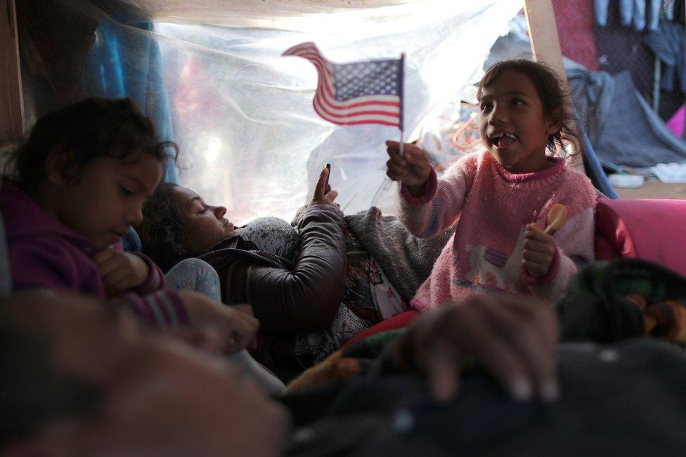 Jeyri, a seven-year-old migrant girl from Honduras, waves a US flag as she rests with her family in a temporary shelter in Tijuana, Mexico, 23 November