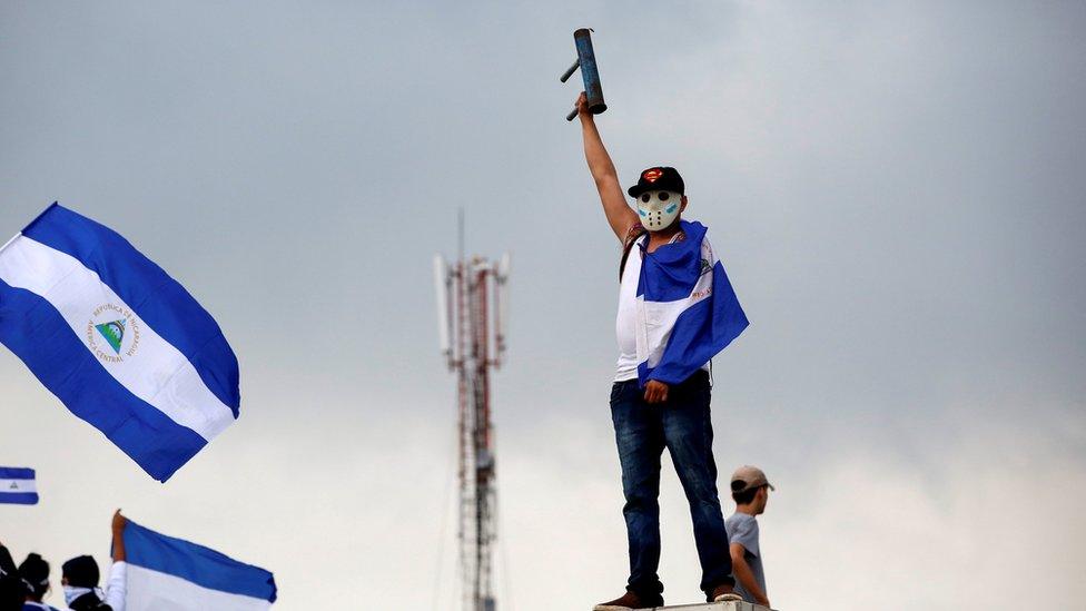 A man wearing a baseball cap, hockey mask, and draped in the national flag raises his home-made mortar in victorious salute in Managua, Nicaragua May 26, 2018.