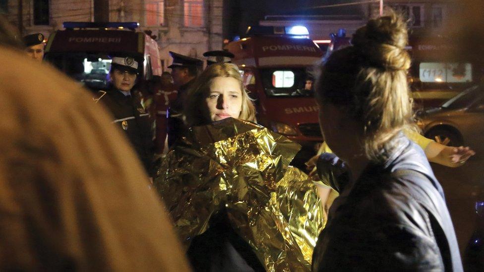 A Romanian woman, survivor of an explosion at a club, looks on as she wears a thermal first aid foil shortly after being rescued by firefighters