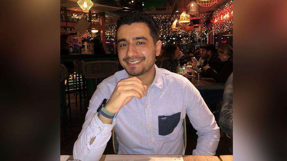 Rustam, a young man sitting in a restaurant wearing a smart blue shirt and smiling at the camera.