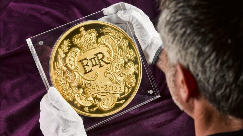 Man holds up huge coin.