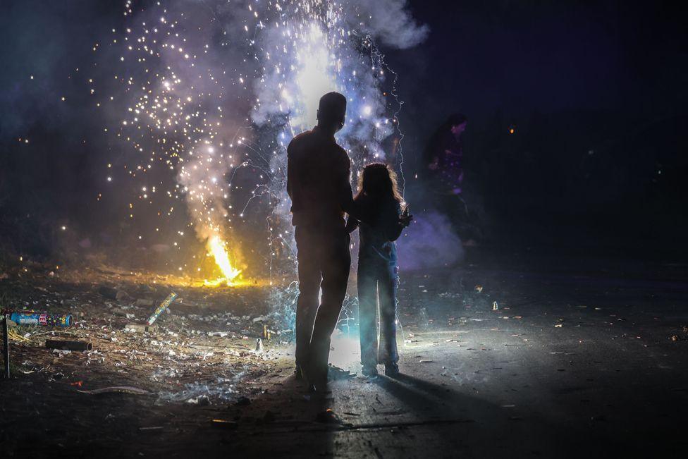 An Ahmedabad night, firecrackers burst like stars, man and child look up