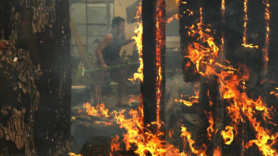 A man battles to save his home pictured through the flames