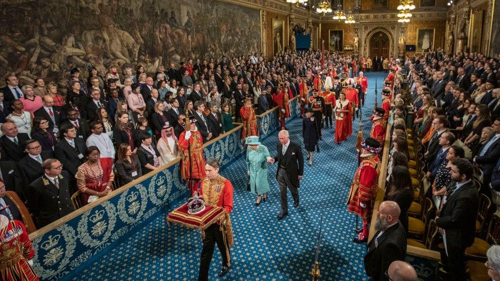 Hundreds of people standing in Parliament and watching the Queen and Prince Charles walk in a procession