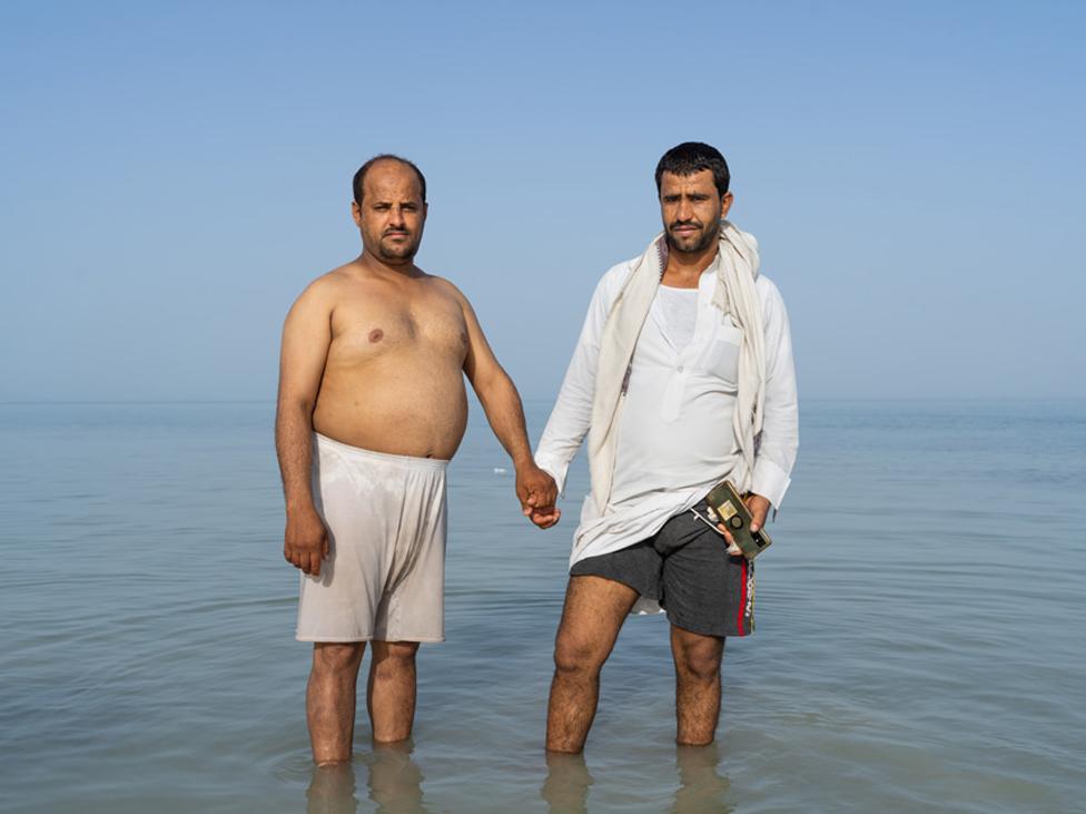 Two men hold hands while standing in the sea