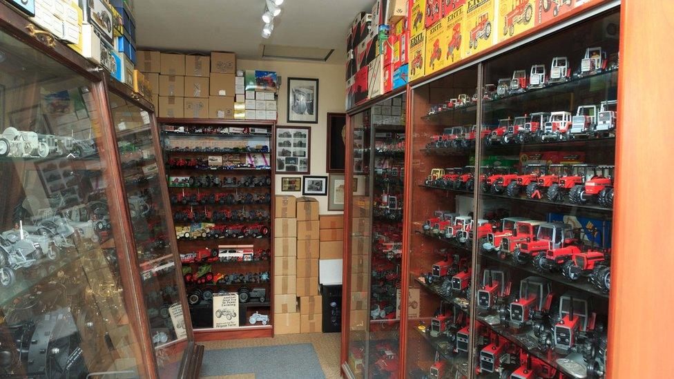 A room featuring glass shelves with tractor models