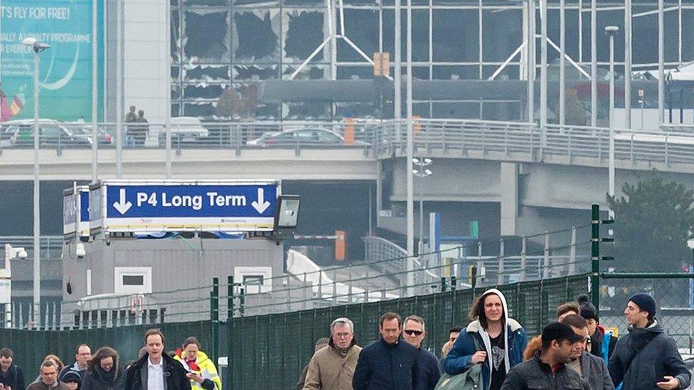 People walk away from the broken windows at Zaventem Airport in Brussels