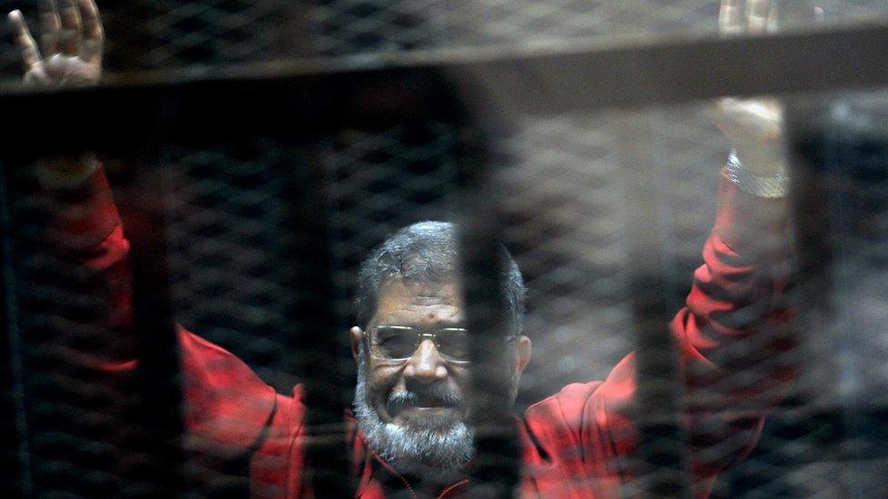 Mohammed Morsi raises his hands inside a cage in a makeshift courtroom at the police academy in Cairo, Egypt (21 June 2015)