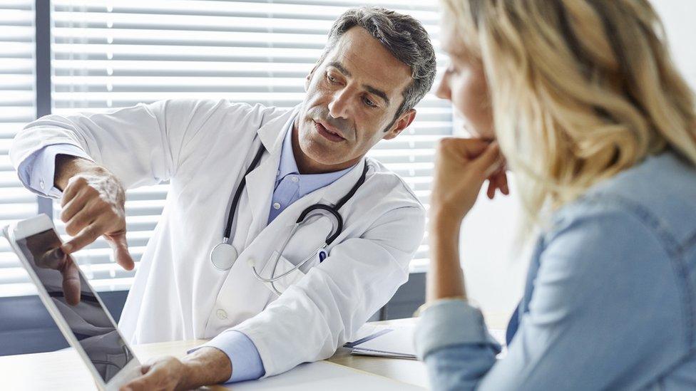 A doctor shows something on a tablet computer to a patient