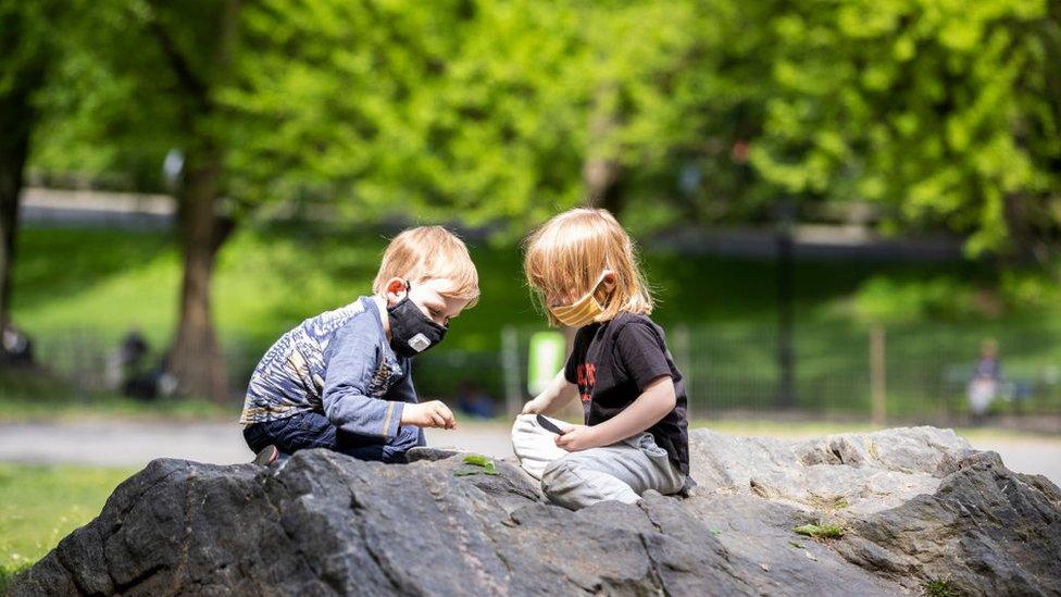 On Memorial Day weekend a two children wear a masks (personal protective equipment) while sitting on the rocks and playing with leaves in Central Park