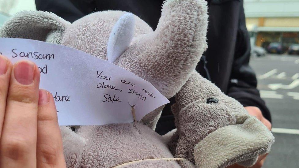 A teddy elephant with a note attached that reads 'you are not alone, stay safe'