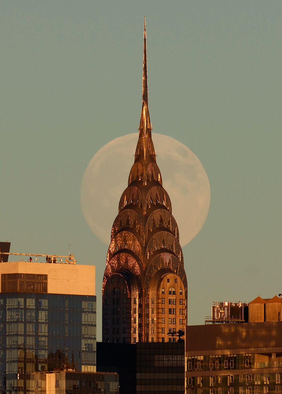 The Beaver Moon rises behind the Chrysler Building as the sun sets in New York City on November 4, 2025, as seen from Hoboken, New Jersey.