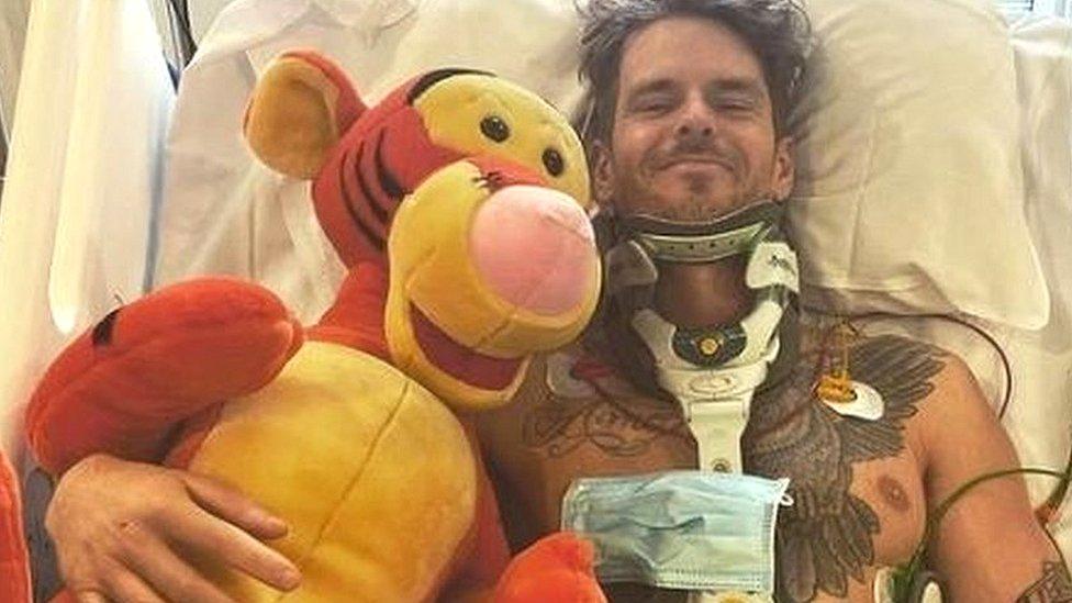 Will in a hospital bed hugging a large stuffed toy