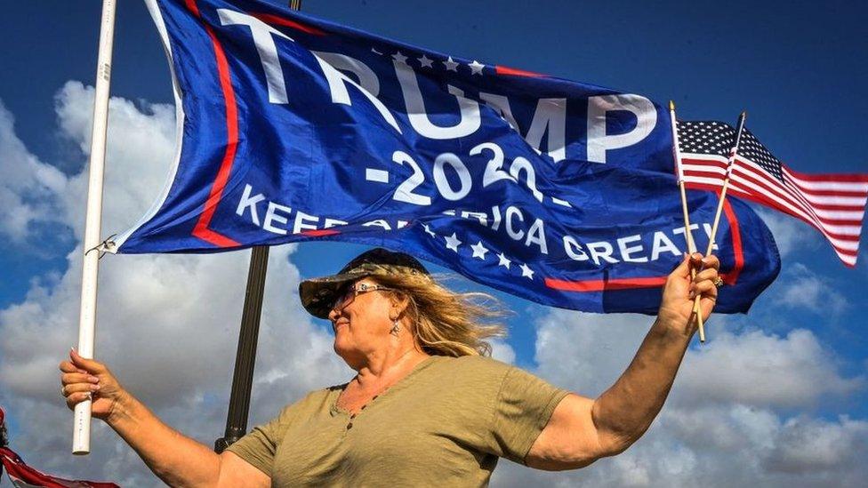 A supporter of Donald Trump holding flags near the Mar-a-Lago estate in Palm Beach, Florida